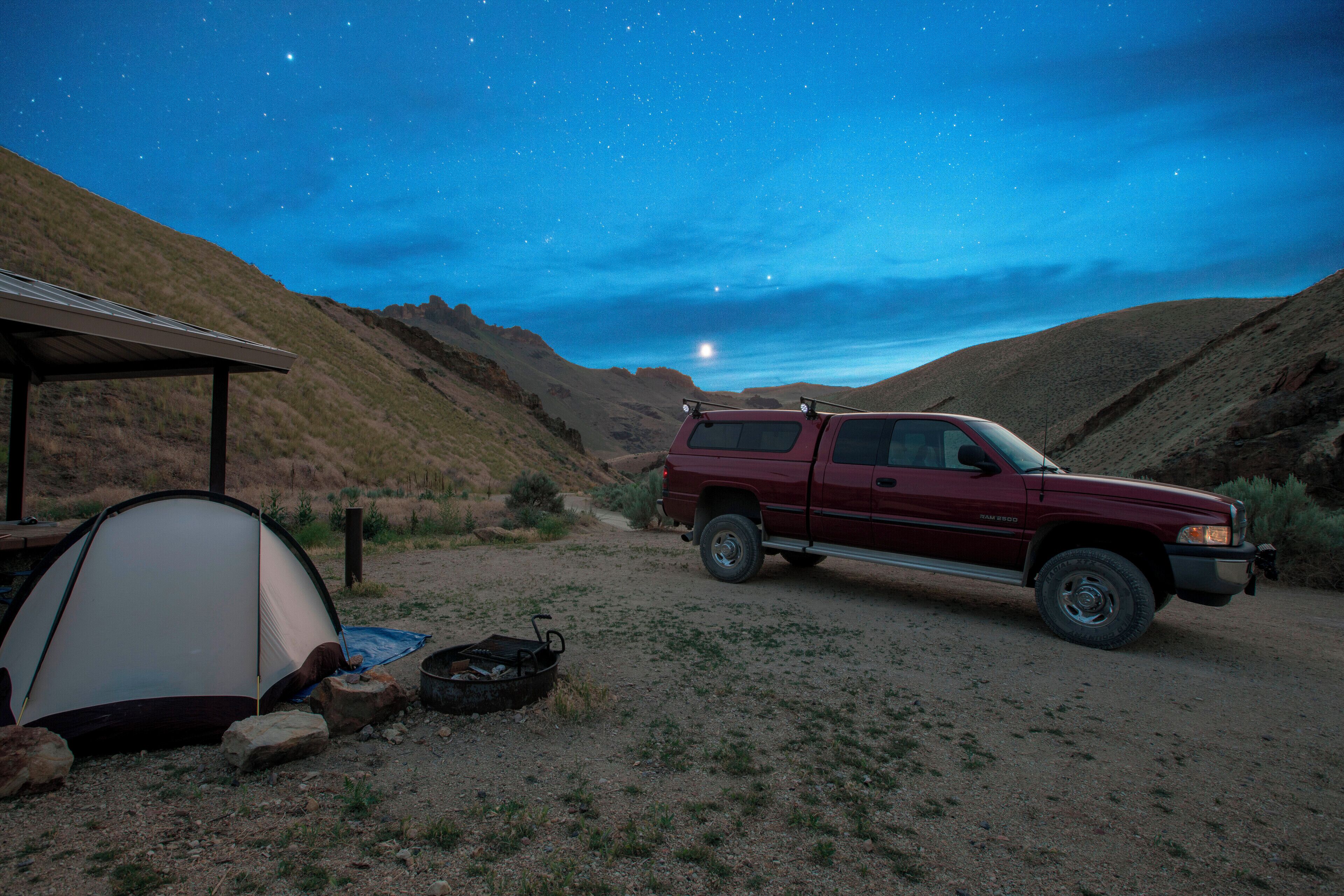 A red truck parked near a tent in a desert at night with stars visible in the sky.
