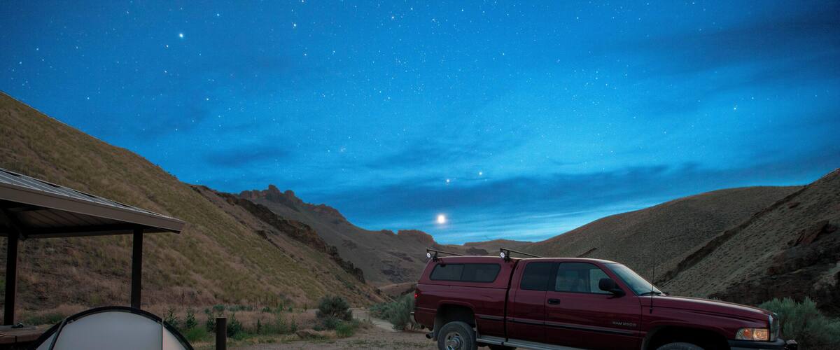 A red truck parked near a tent in a desert at night with stars visible in the sky.