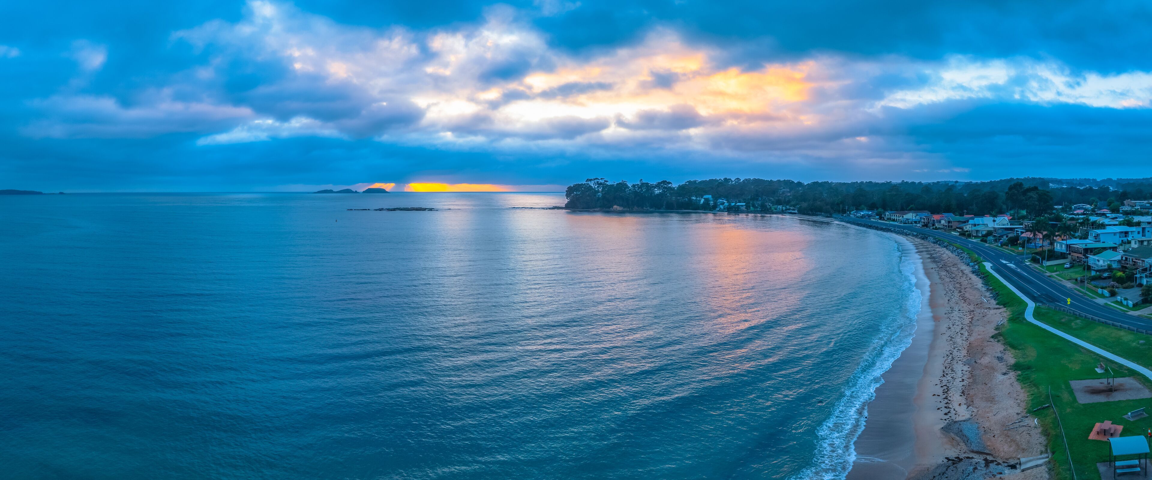 A coastal landscape with a beach, a road, and a distant sunset.