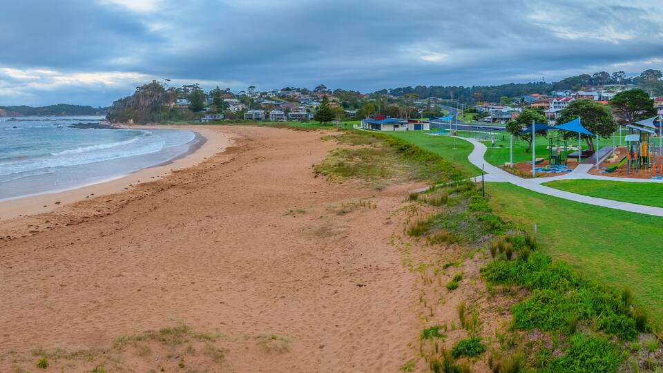 A beach with a playground and houses in the background.