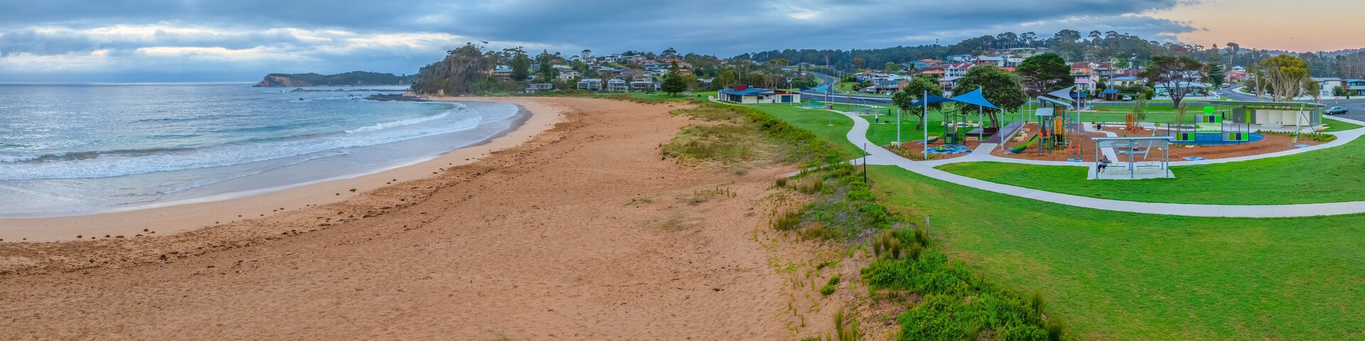 A beach with a playground and houses in the background.