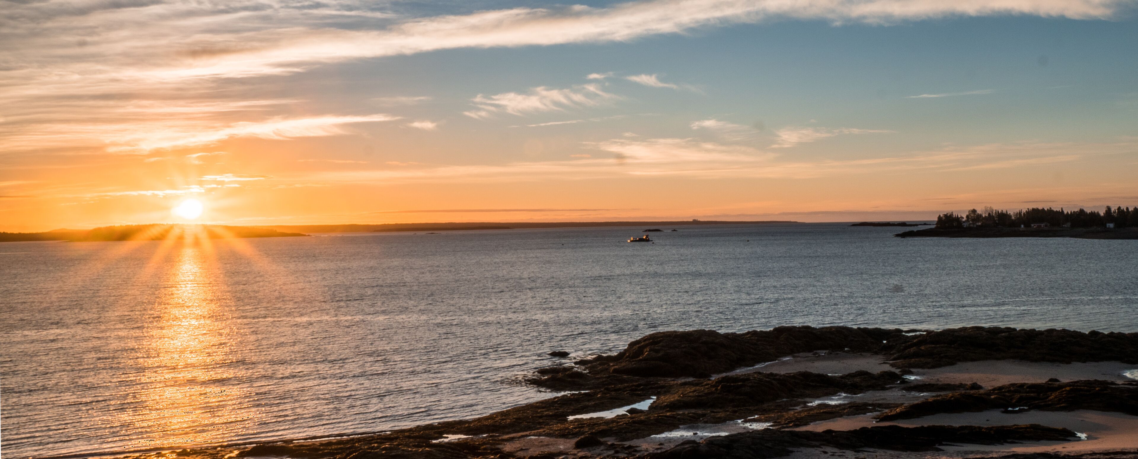 A sunset over a calm sea with rocky shores and a distant shoreline.