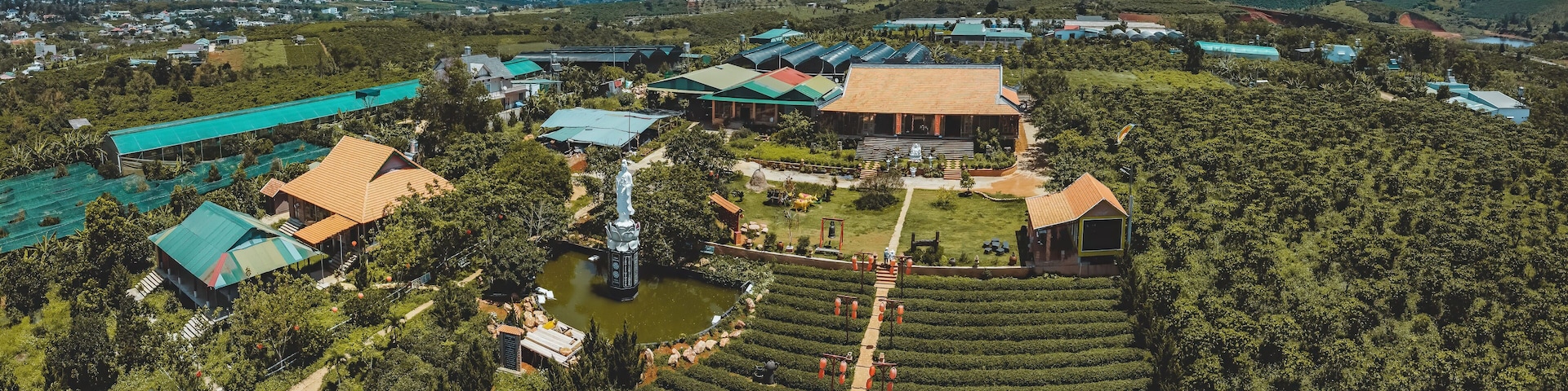 Vista aérea de una zona rural con campos en terrazas, un edificio grande con techo verde y una estatua en el centro.