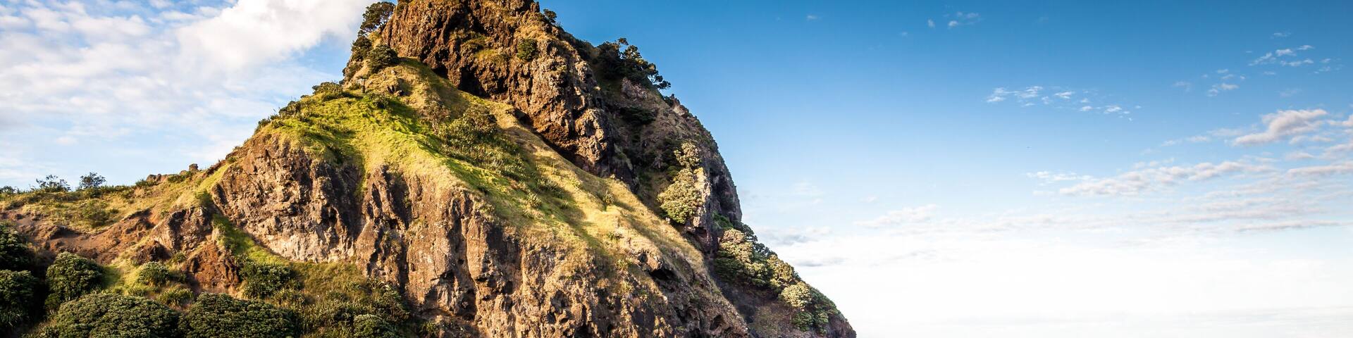A coastal landscape with a prominent rocky cliff, a sandy beach, and the ocean.
