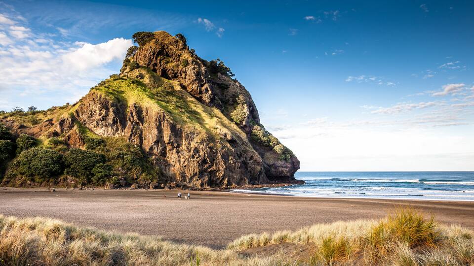 A coastal landscape with a prominent rocky cliff, a sandy beach, and the ocean.