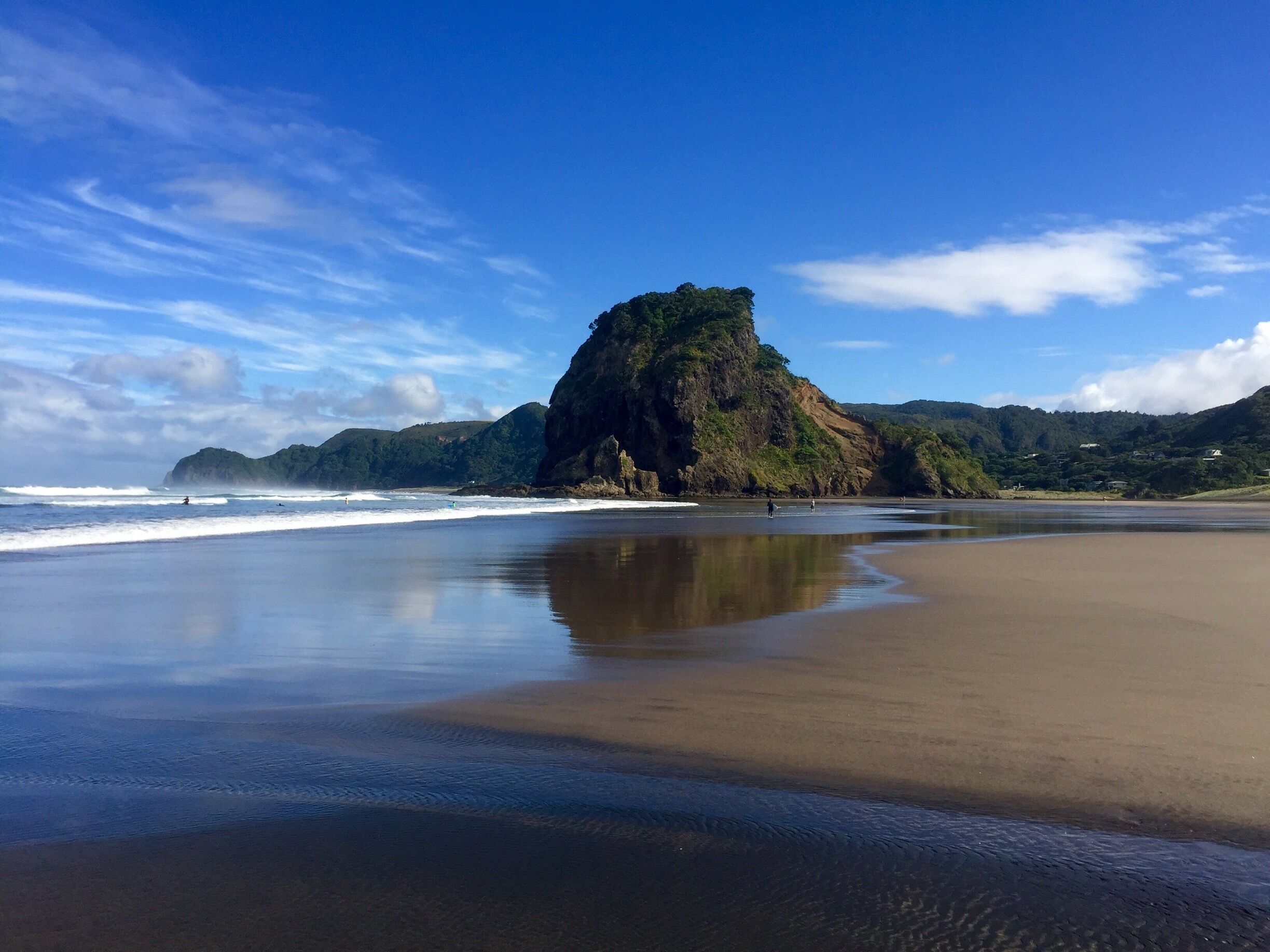 A beach with a large rock formation and waves crashing onto the shore.