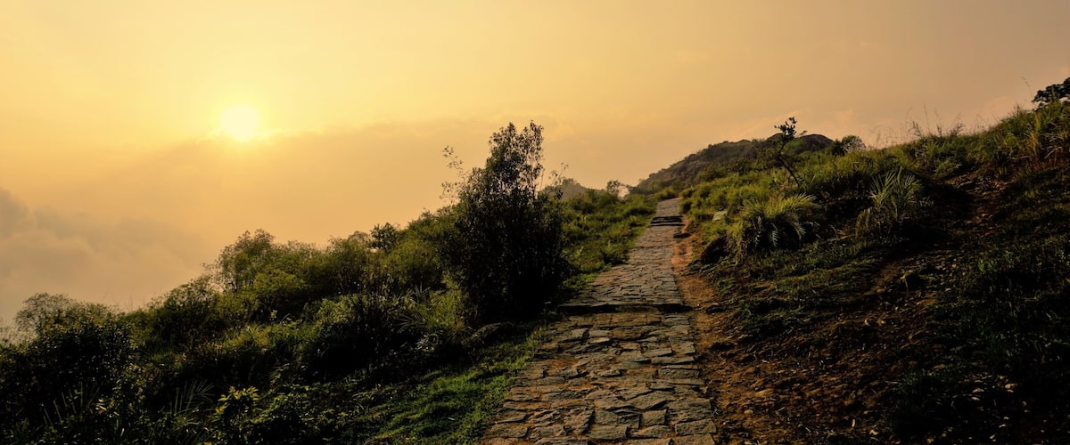 A stone pathway ascending a grassy hill with the sun setting in the background.