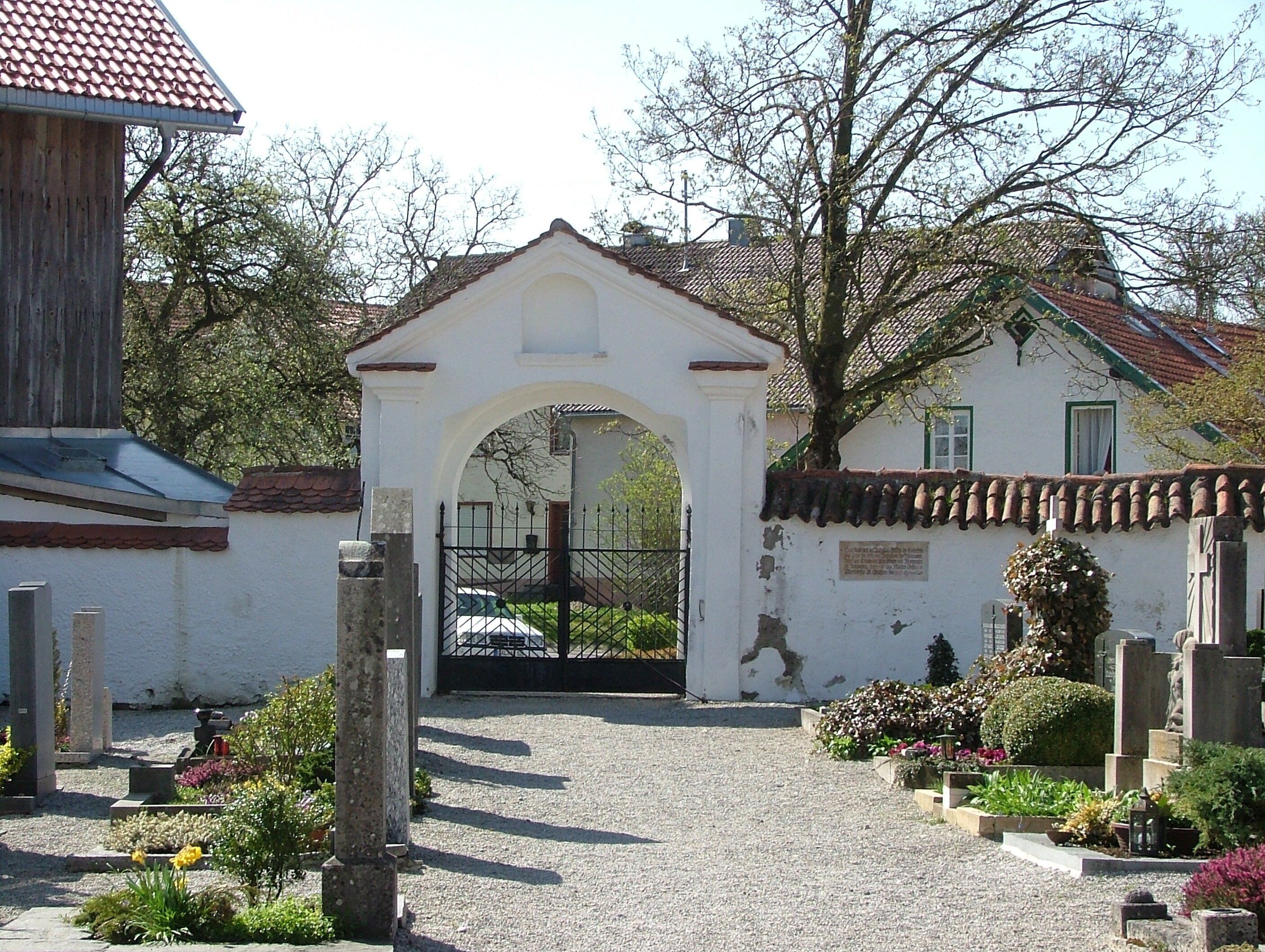 A cemetery entrance with a white archway, a black gate, and a white building with a tiled roof.