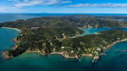 Aerial view of Kawau Island, New Zealand. Lush green islands are surrounded by turquoise water. Sailboats dot the bays, creating a scenic coastal landscape.