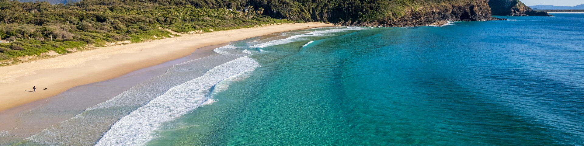 Una playa con aguas turquesas cristalinas, una orilla arenosa y una colina boscosa al fondo.