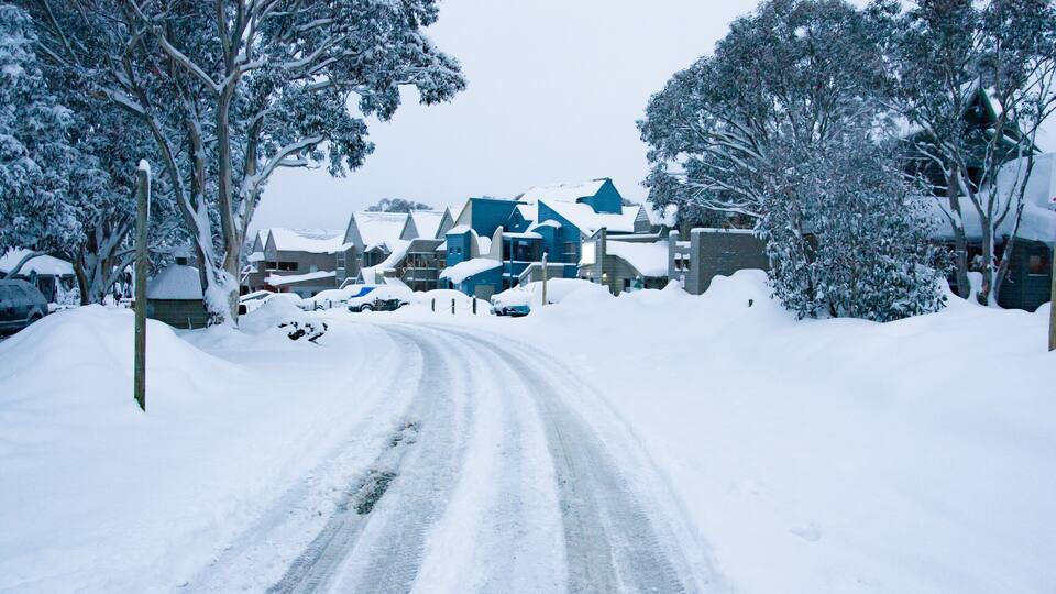 A snow-covered road leading to a cluster of houses with blue roofs.