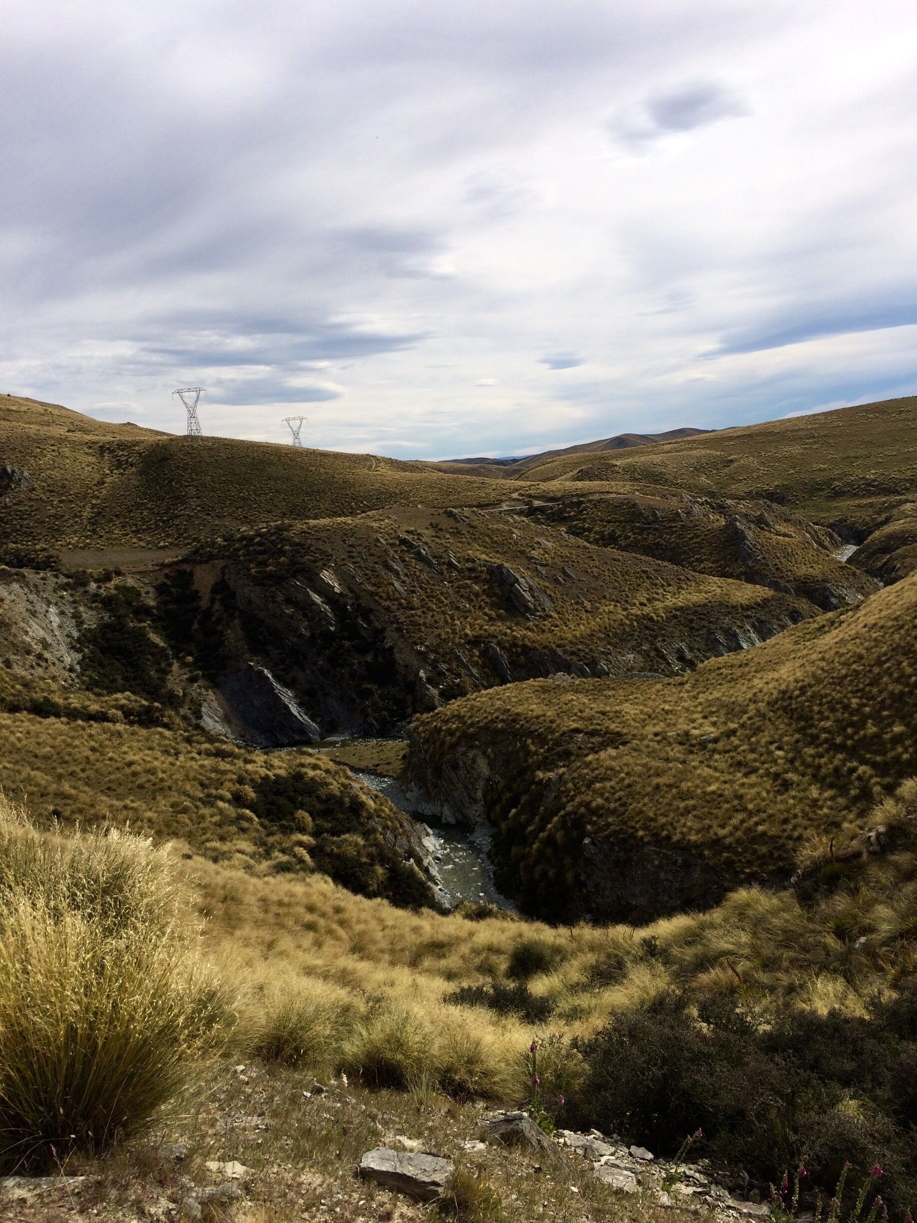 A rugged landscape with rolling hills, a small stream, and power lines in the distance.
