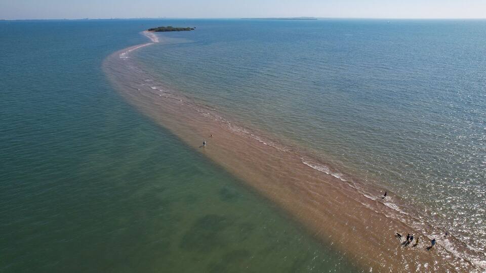 A coastal landscape with a sandy beach, clear water, and a distant island.
