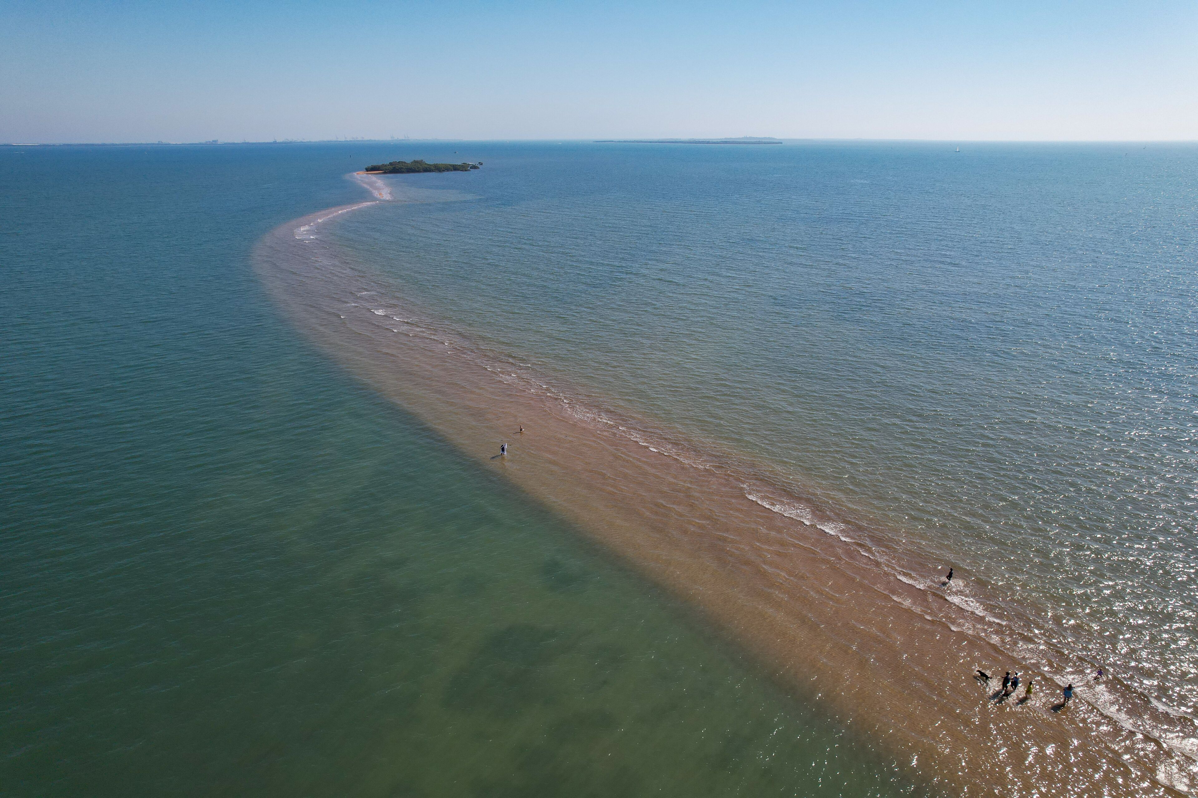 A coastal landscape with a sandy beach, clear water, and a distant island.