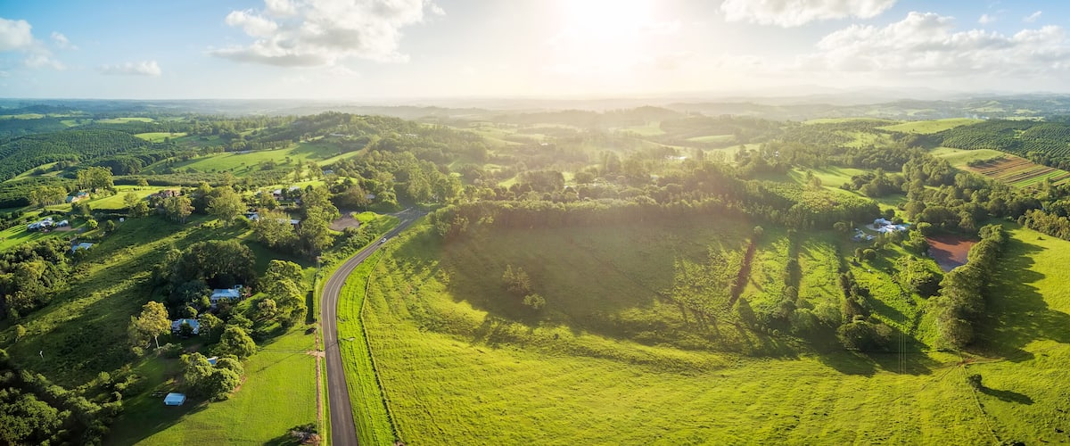 A lush green valley with a winding road, scattered houses, and dense forests.