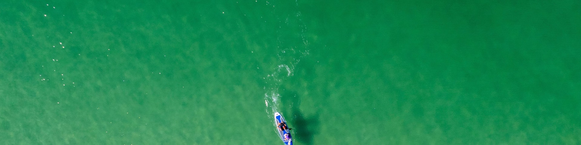 A beach with clear turquoise water and a surfer riding a wave.