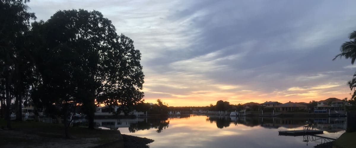 A calm lake at sunset with reflections of trees and buildings.