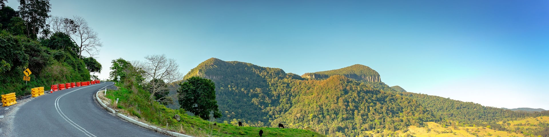A winding road with orange barriers, a mountain with a castle, and a clear blue sky.