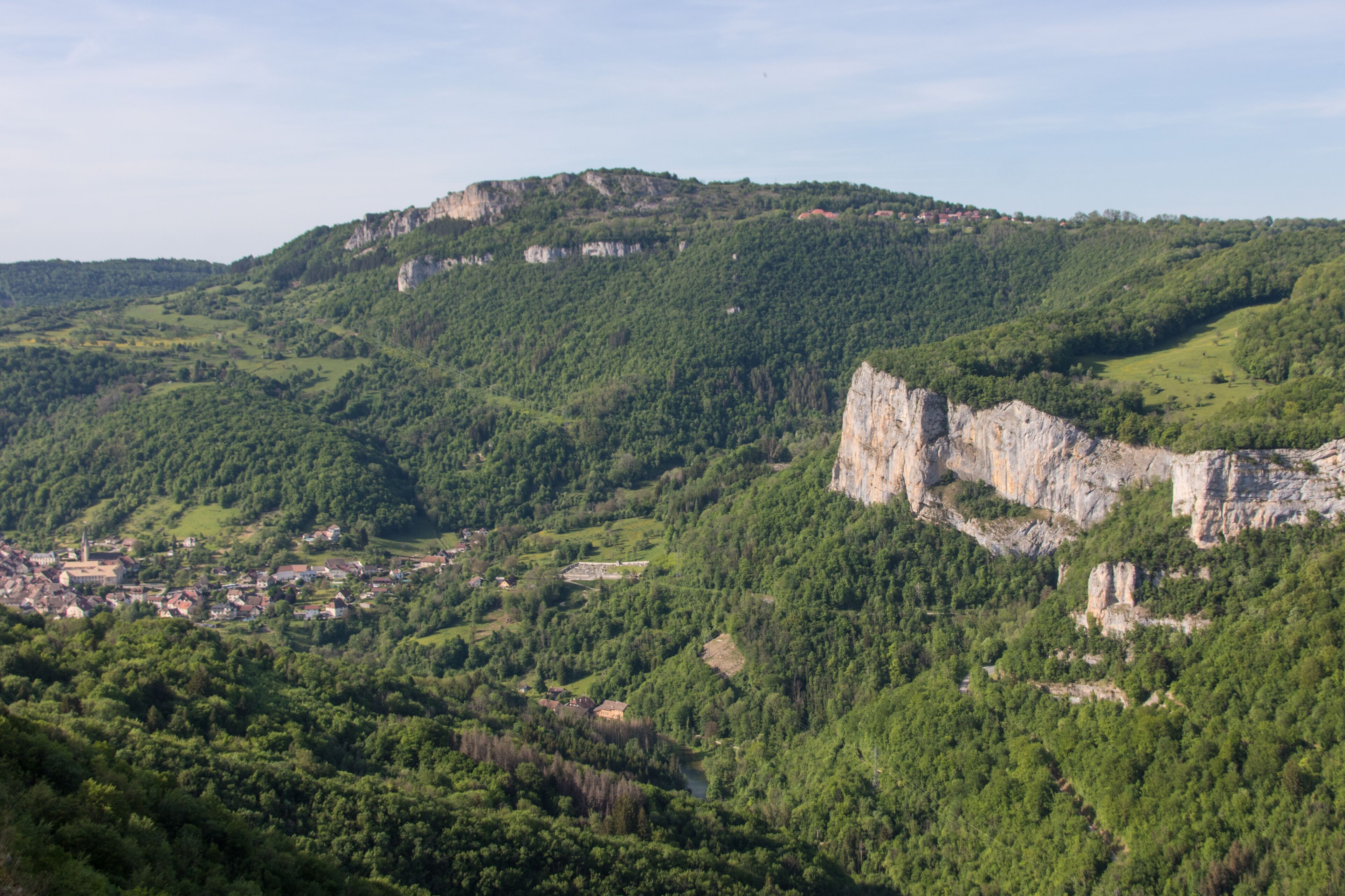 A mountainous landscape with a village nestled at its base, surrounded by dense forests and rocky cliffs.
