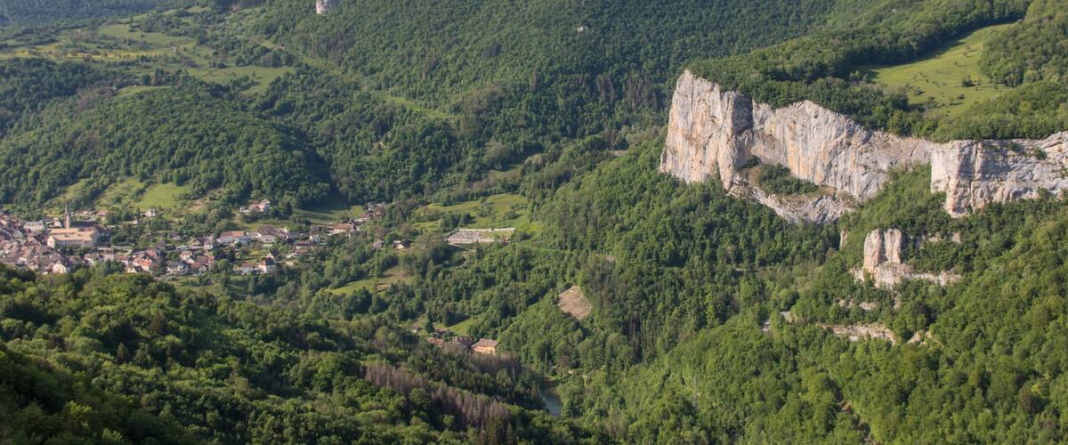 A mountainous landscape with a village nestled at its base, surrounded by dense forests and rocky cliffs.