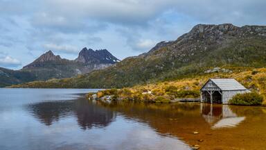 A tranquil lake with a wooden structure on the shore, surrounded by rugged mountains and sparse vegetation.