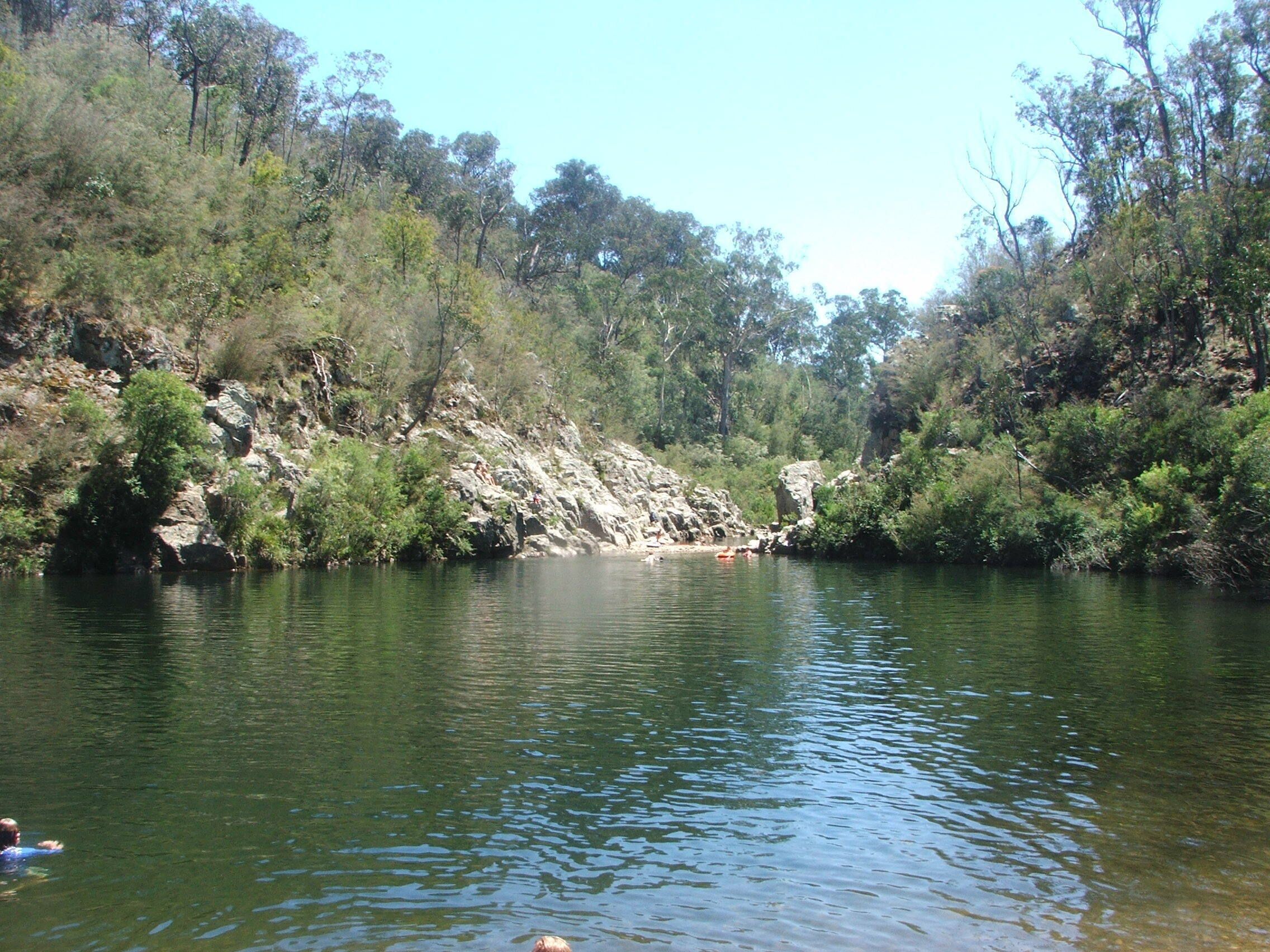 A calm river surrounded by dense greenery and rocky terrain.