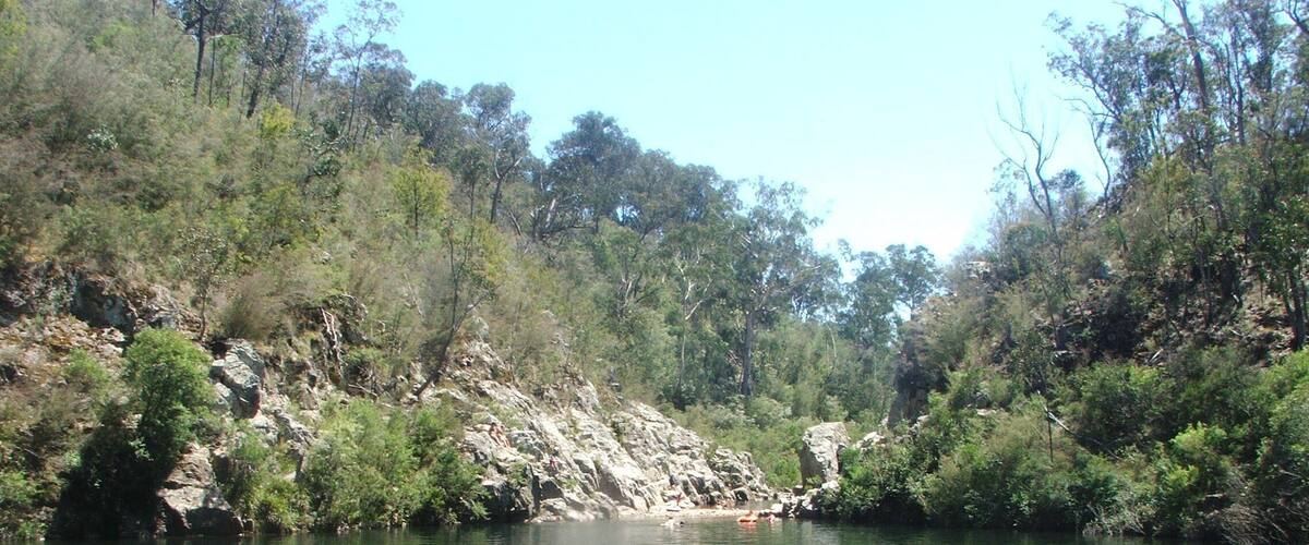 A calm river surrounded by dense greenery and rocky terrain.