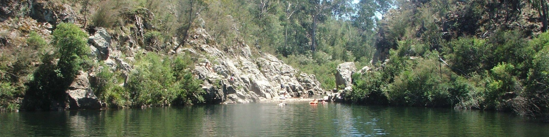A calm river surrounded by dense greenery and rocky terrain.