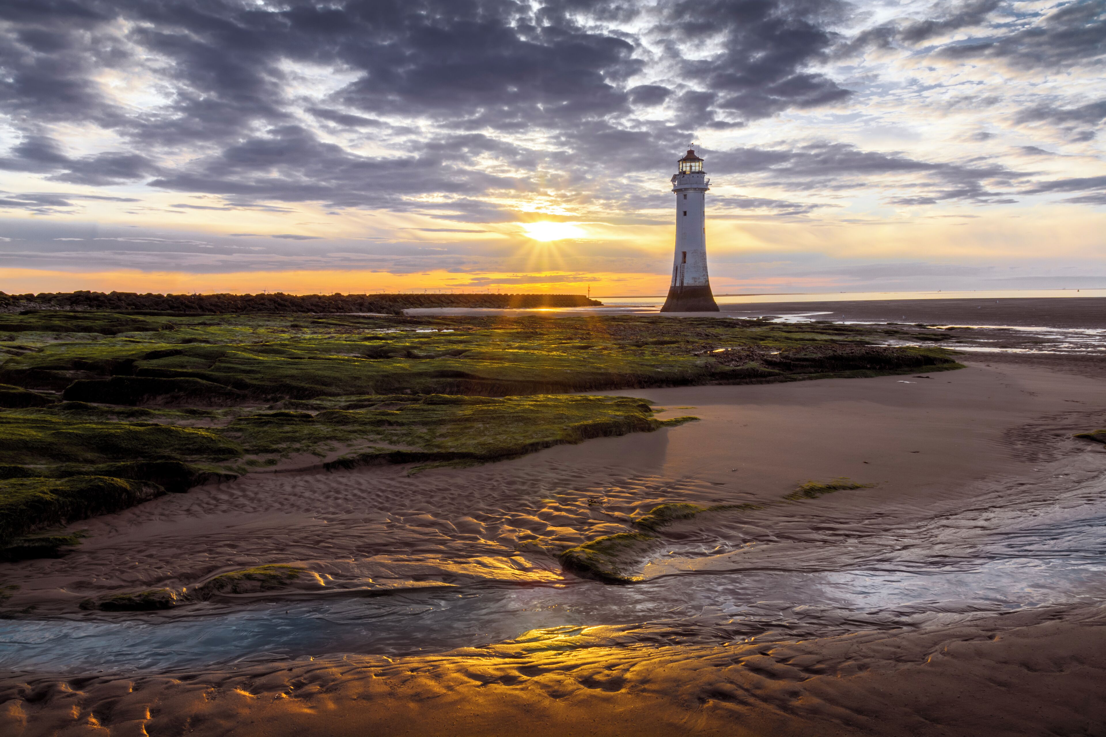Ein Leuchtturm an einem Strand, im Hintergrund ein Sonnenuntergang.