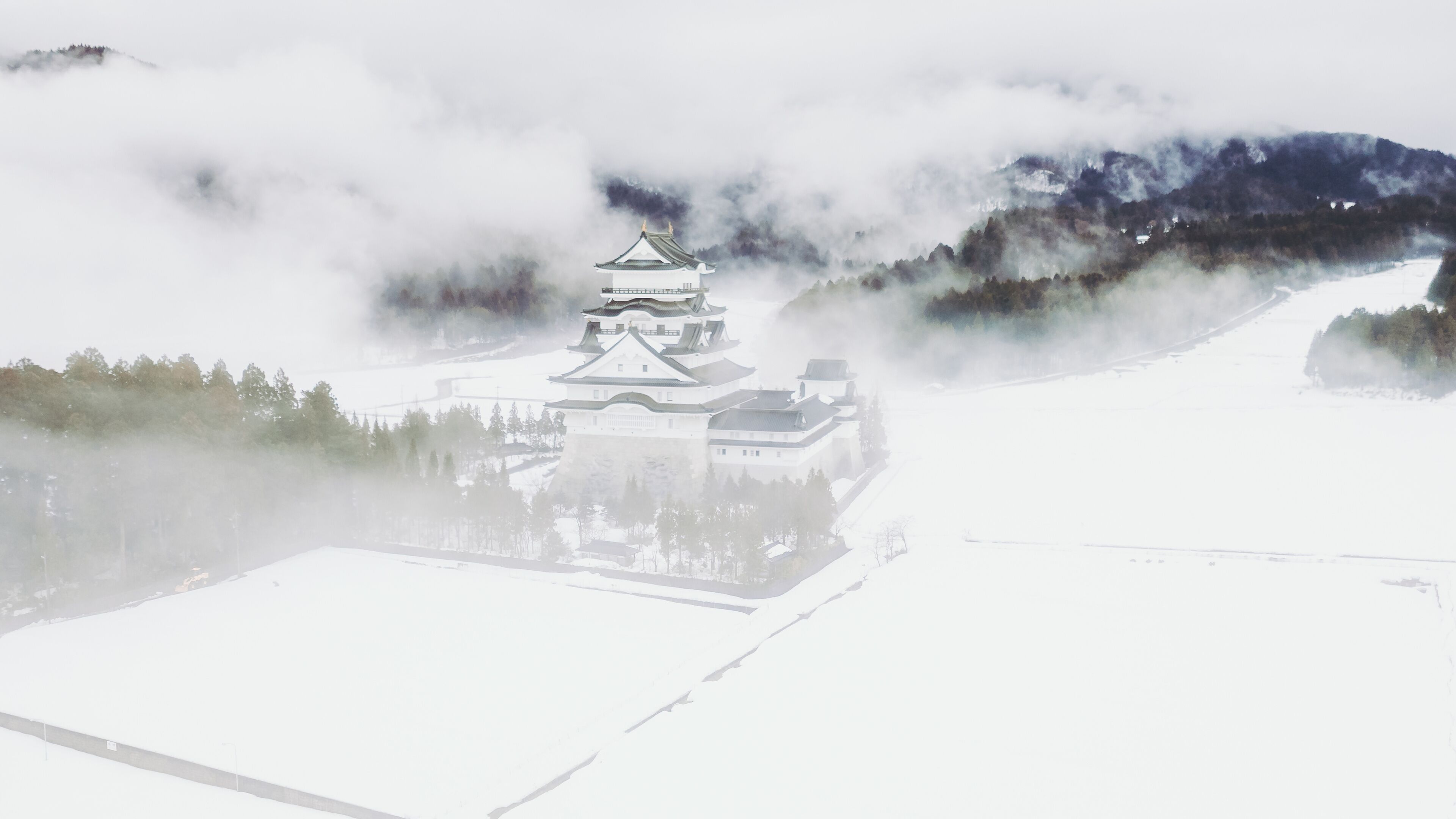 Aerial view of Katsuyama Castle Museum emerges from the snow-covered landscape, its white walls contrasting against the misty mountains, Katsuyama, Fukui, Japan.