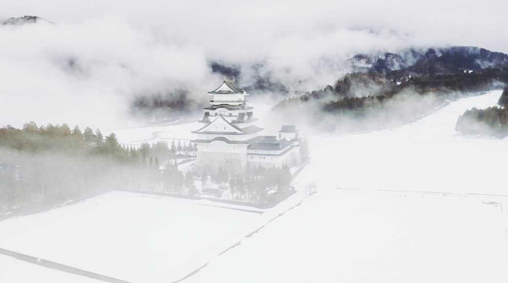 Aerial view of Katsuyama Castle Museum emerges from the snow-covered landscape, its white walls contrasting against the misty mountains, Katsuyama, Fukui, Japan.