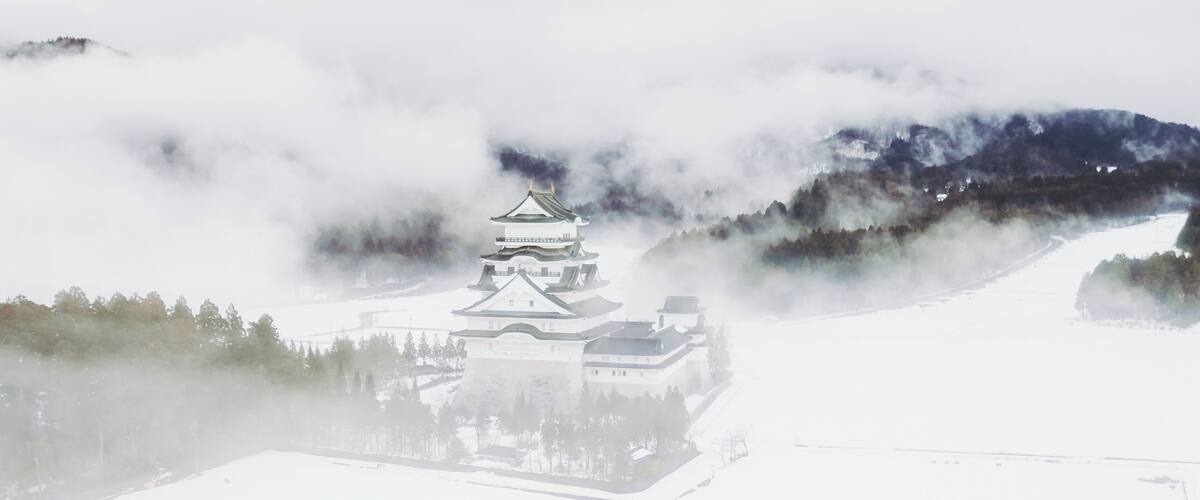 Eine traditionelle japanische Burg, umgeben von verschneiter Landschaft und Bergen.