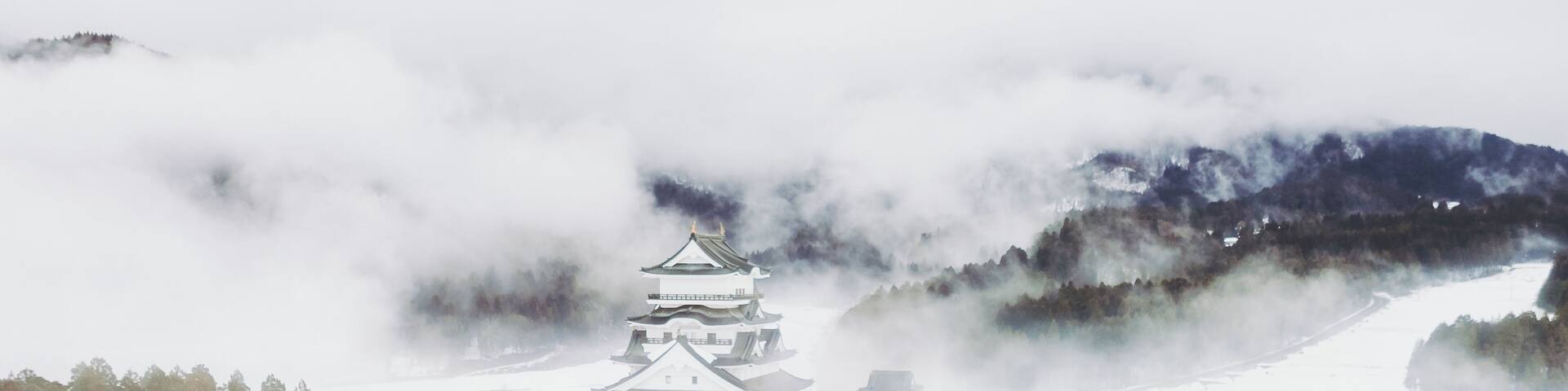 A traditional Japanese castle surrounded by snow-covered landscape and mountains.
