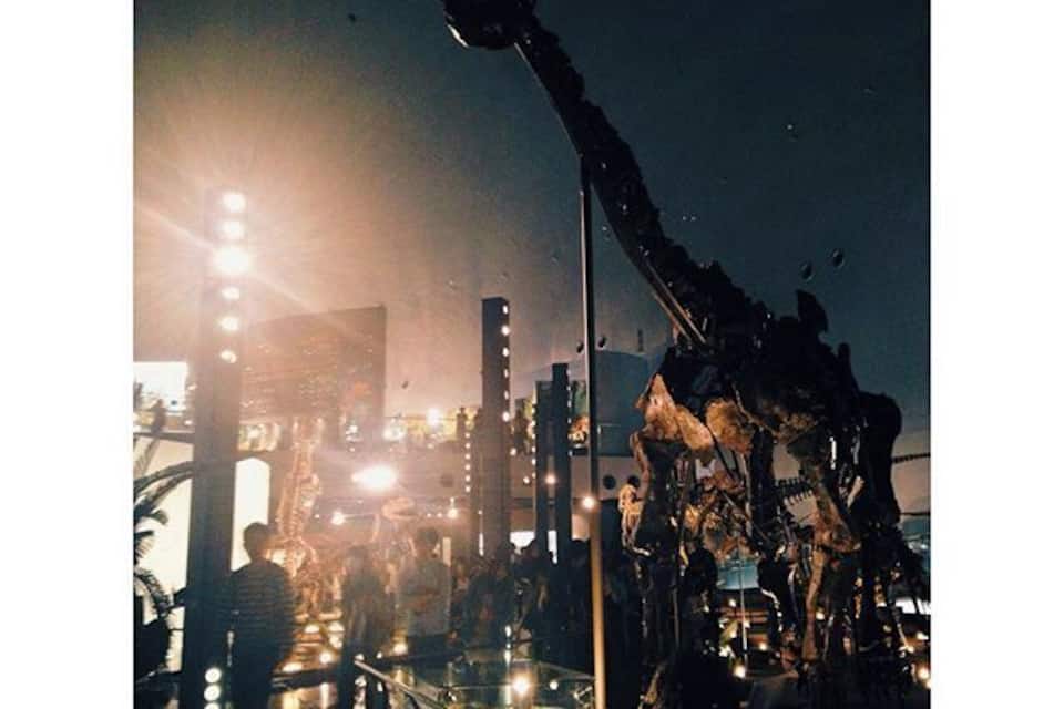 A large dinosaur sculpture in an urban setting at night.