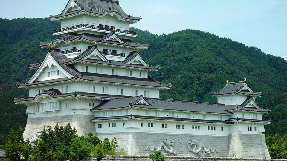 A traditional Japanese castle with multiple tiers and golden statues on top, surrounded by lush green hills.