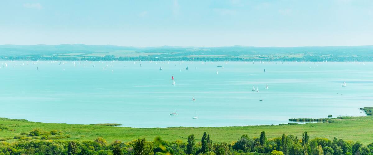 A coastal landscape with a large body of water, sailboats, and green fields.