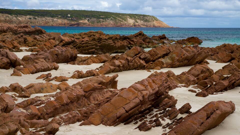 A rocky beach with large boulders and a clear blue sea.