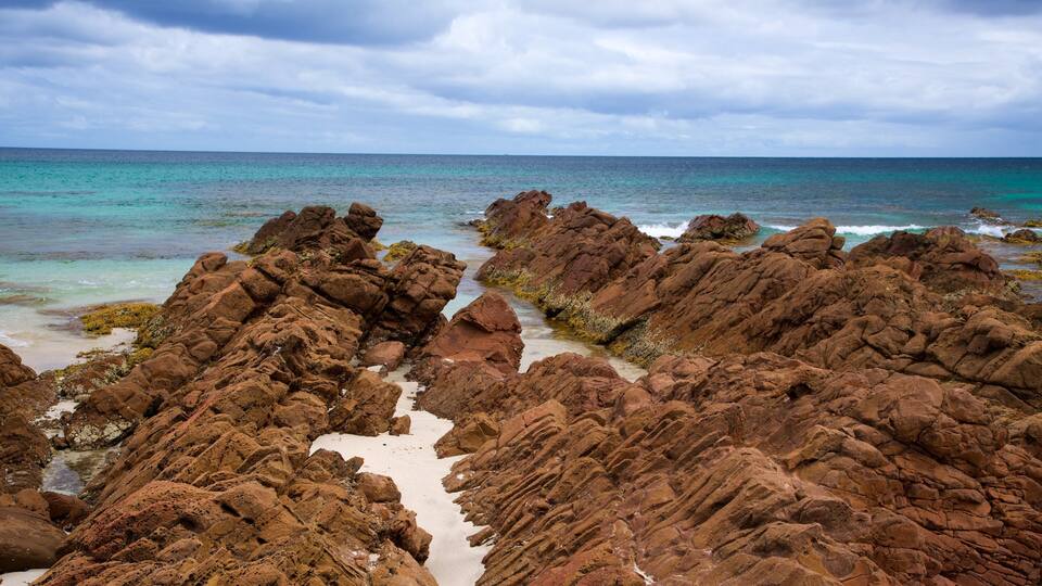 A rocky coastline with clear turquoise waters and a cloudy sky.
