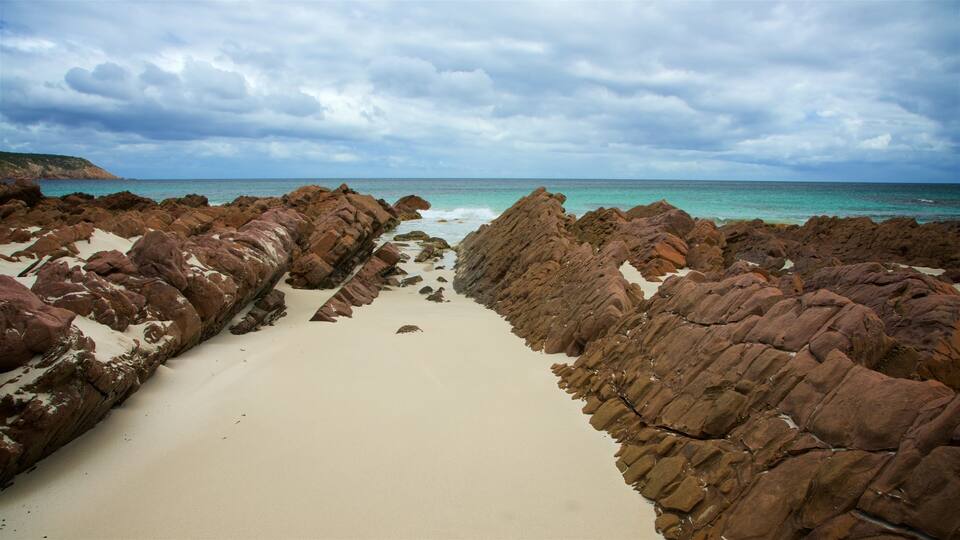 A rocky beach with white sand and turquoise water under a cloudy sky.