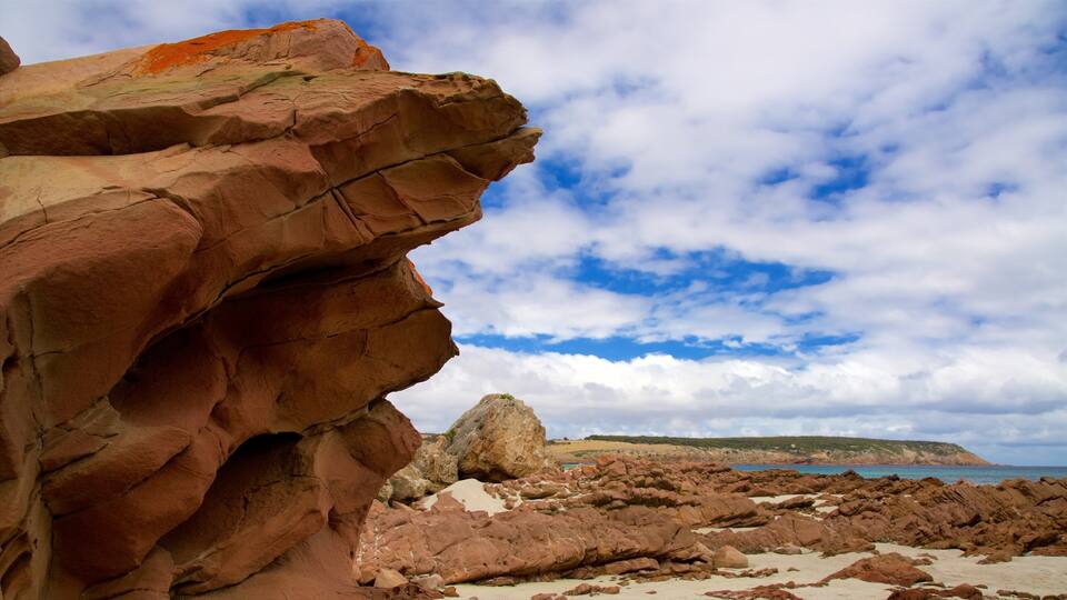 A rocky coastline with a prominent red rock formation and a distant view of the sea under a partly cloudy sky.