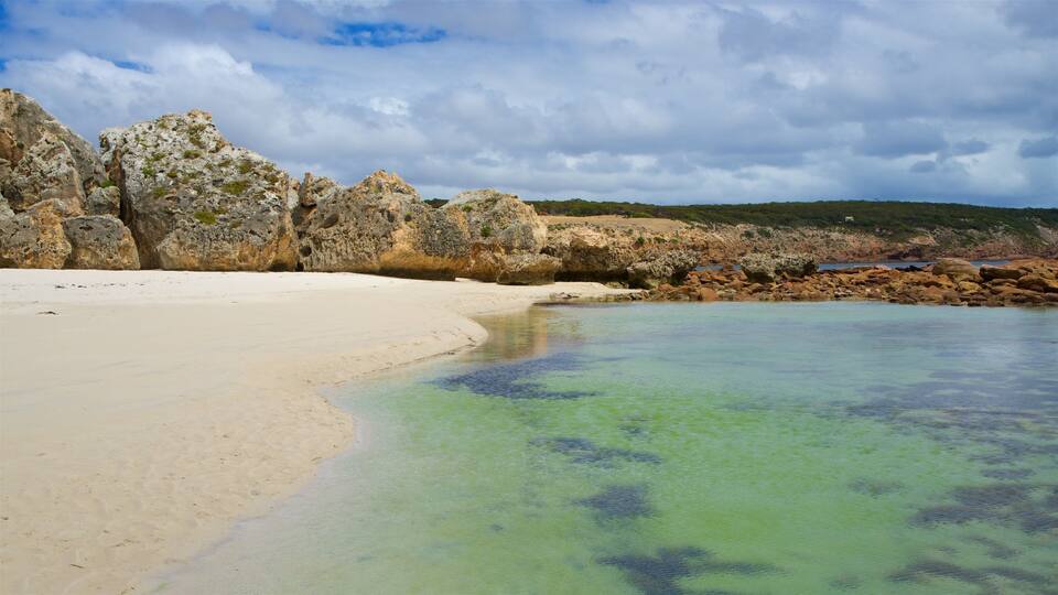 A beach with clear turquoise water, white sand, and rocky outcrops.