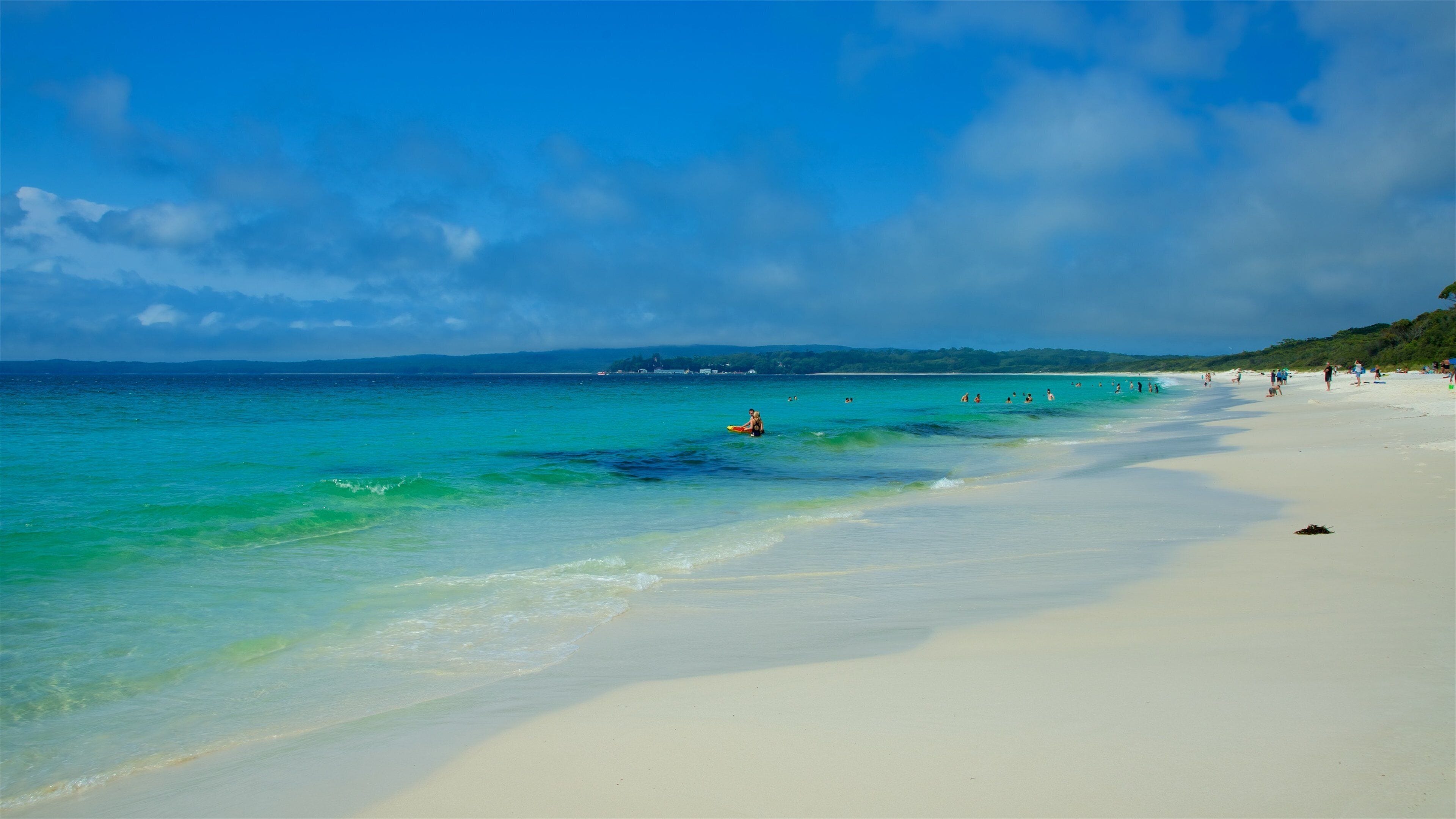 A beach with clear turquoise water, white sand, and a few people in the water.