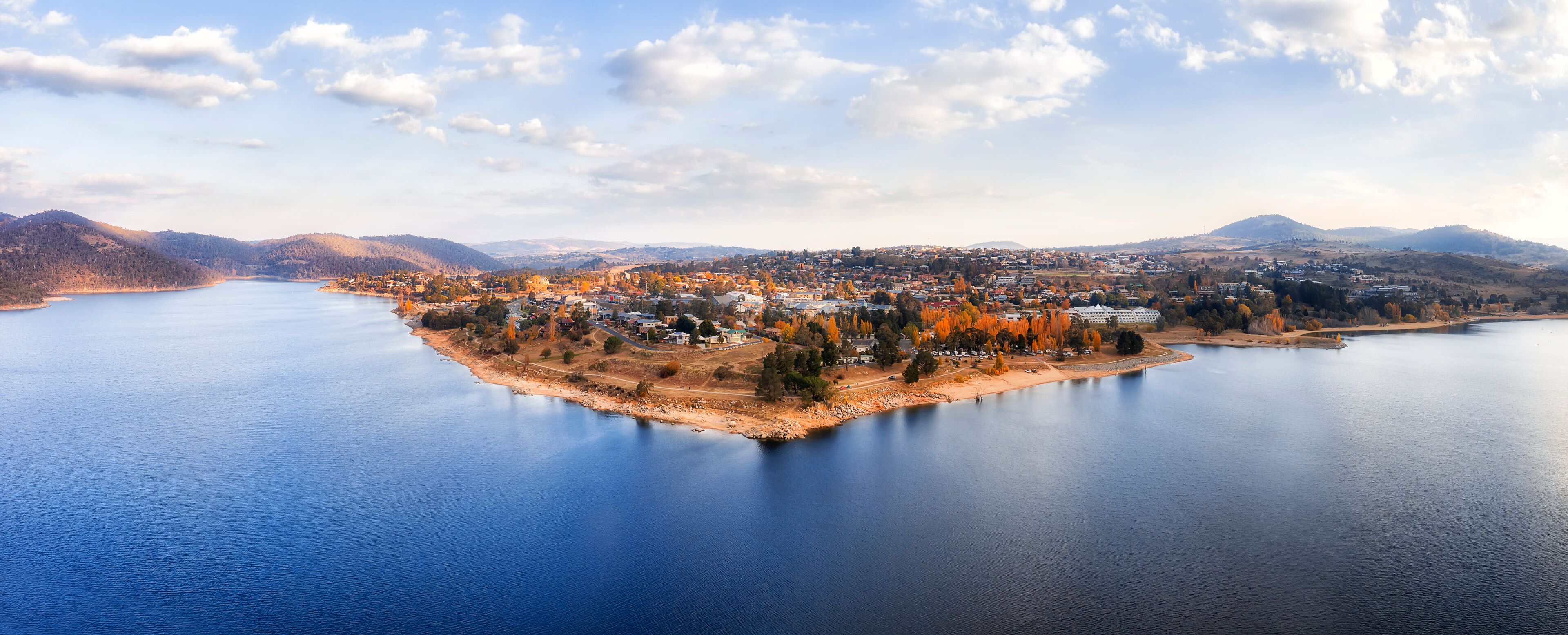 A lake surrounded by a town with autumn-colored trees and hills in the background.