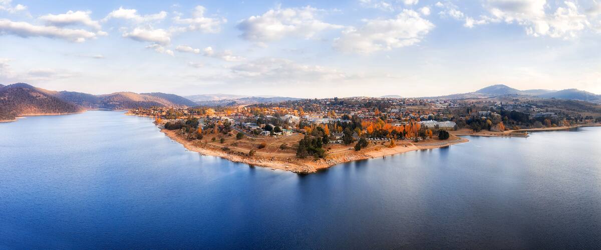A lake surrounded by a town with autumn-colored trees and hills in the background.