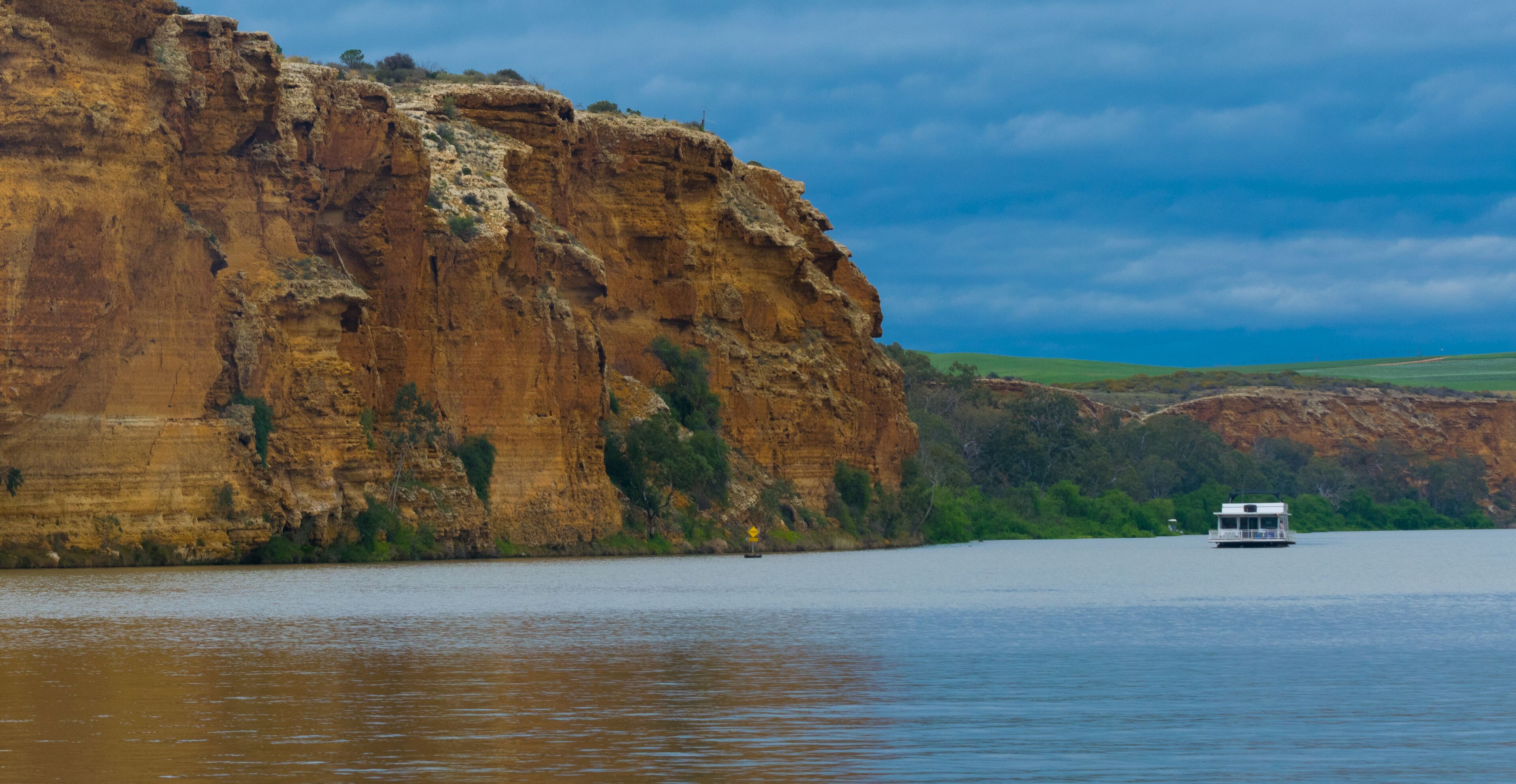 A river with a boat, a large cliff, and green hills in the background.