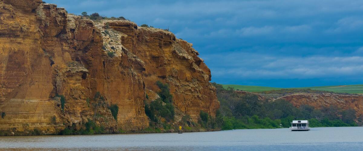 A river with a boat, a large cliff, and green hills in the background.