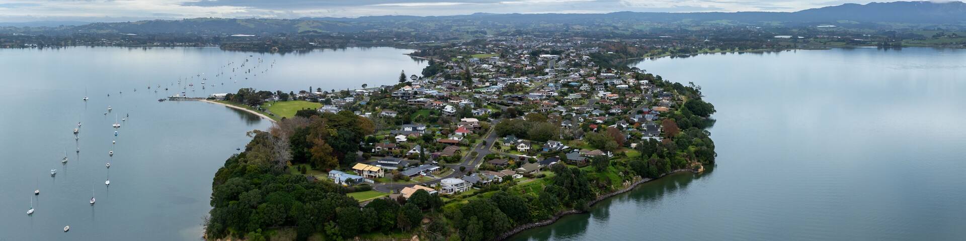 Aerial view of a peninsula with houses and boats in a bay in Omokoroa, Bay Of Plenty, New Zealand. The image shows the beauty of the landscape and the lifestyle of the people who live there.