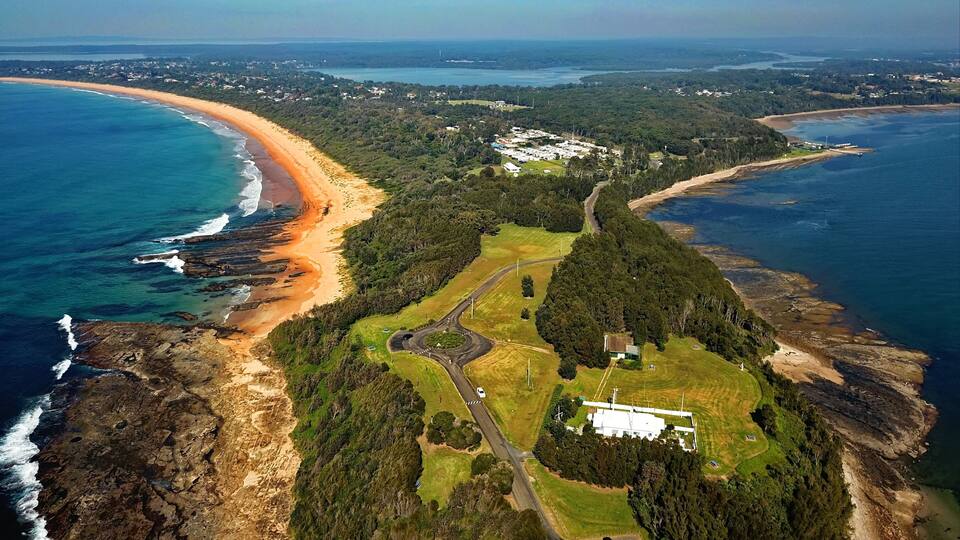 A coastal landscape with a beach, a winding road, and a large building complex.