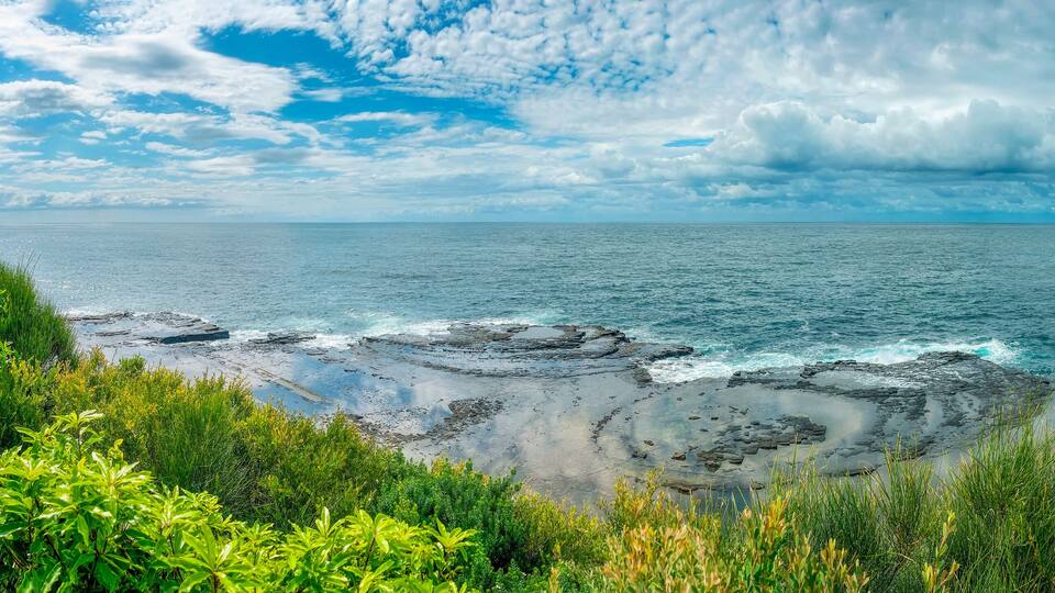 A coastal landscape with rocky shores, green vegetation, and a clear blue sky.