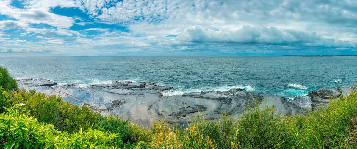 A coastal landscape with rocky shores, green vegetation, and a clear blue sky.
